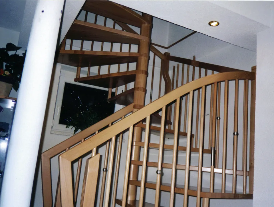 Wendeltreppe aus hellem Holz mit Rundstabgeländer und Edelstahlknöpfen